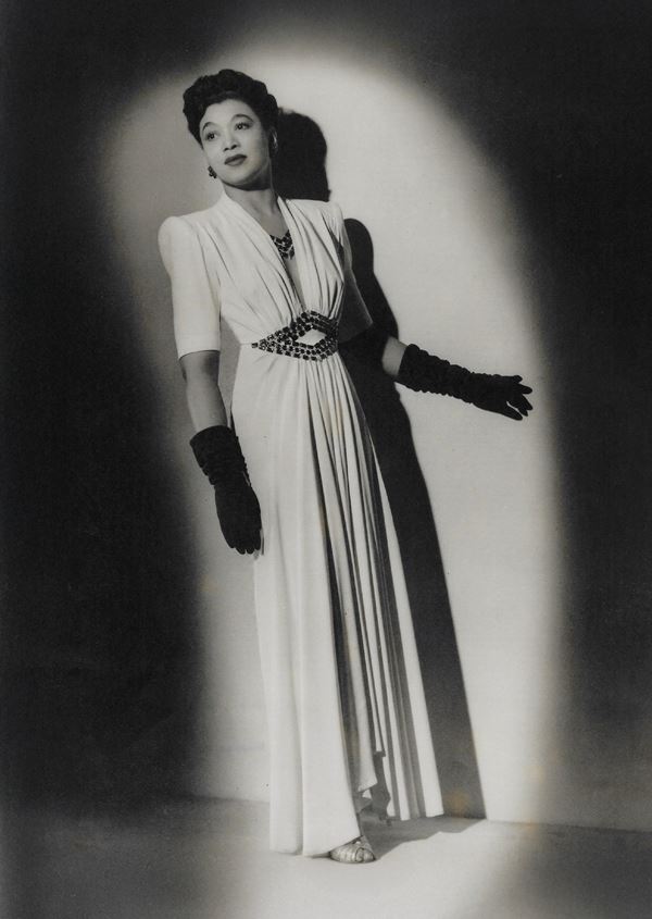 Black & white photo of an elegant black woman in a white dress and long gloves.